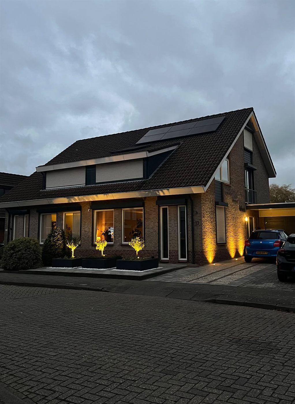 Vrijstaande woning bij schemering met verlichte boompjes, gevel en entree