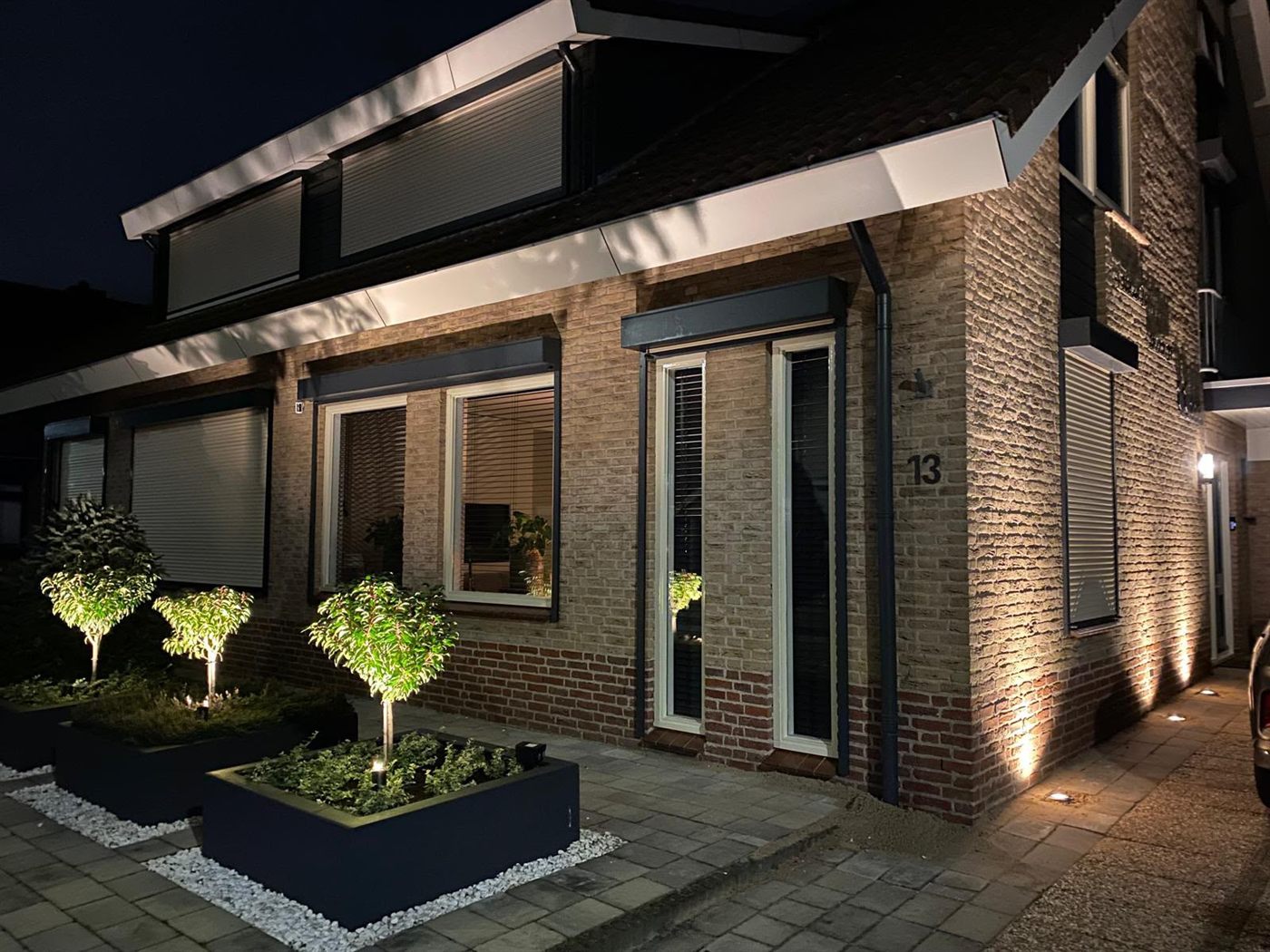Warme grondspots op de gevelhoek en boompjes bij de voordeur