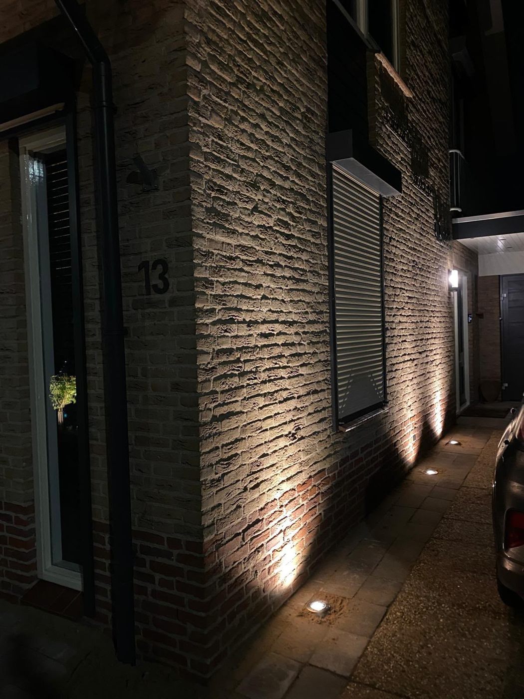 Grondspots die 's nachts de zijgevel uitlichten en de textuur van de steen tonen